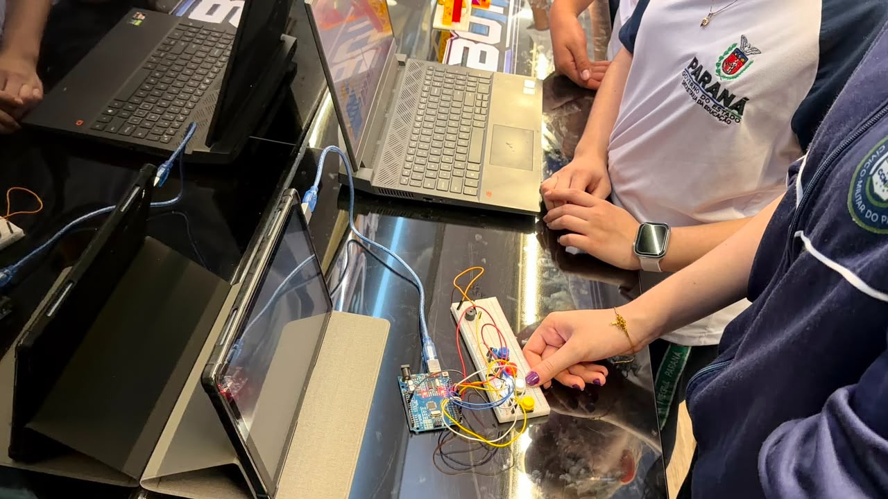 Aluna montando um circuito em protoboard ao lado de notebooks com o Arduino conectado