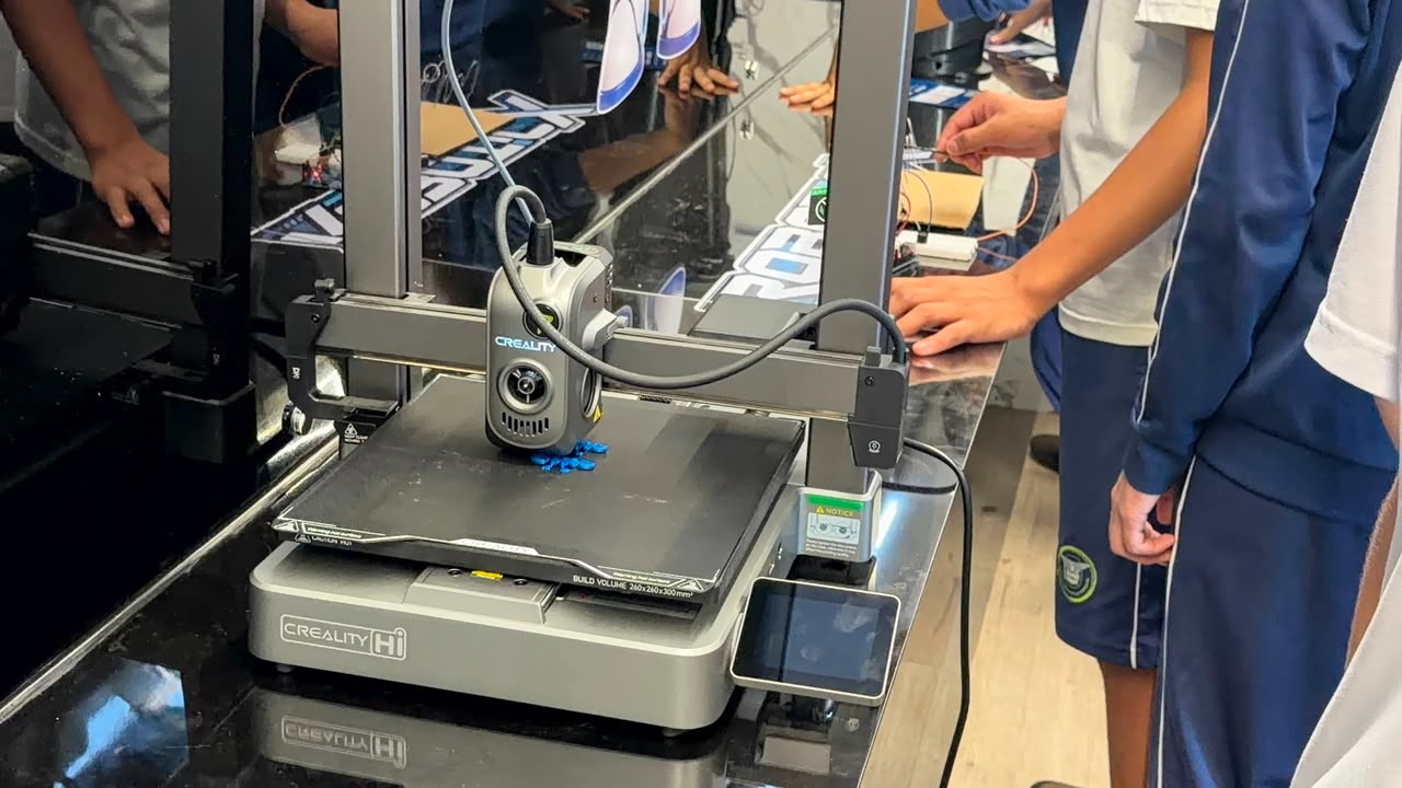 Impressora 3D Creality imprimindo peças azuis enquanto alunos acompanham