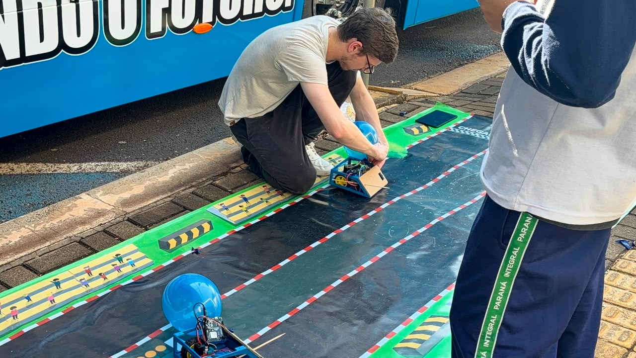 Instrutor da RoboticX conduzindo o desafio da pista com alunos ao lado do ônibus-laboratório